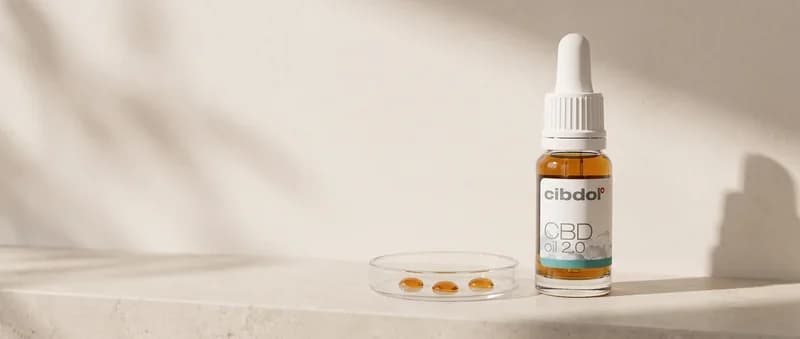A white dropper bottle beside a small glass dish holding three amber oil drops on a stone ledge