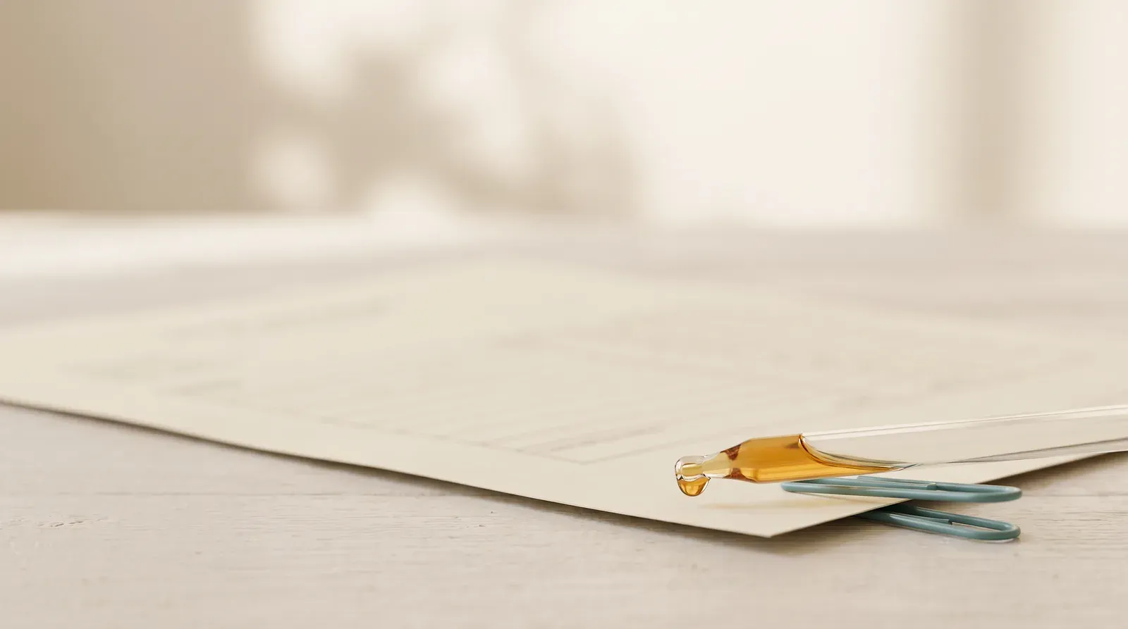 A glass pipette with a drop of amber oil resting on a printed certificate